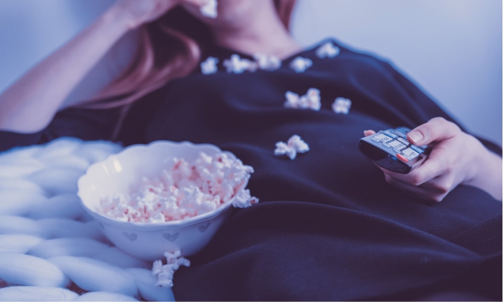 Jeune femme qui regarde la télévision depuis son canape avec un bol de popcorns